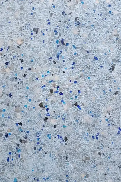 Close-up of exposed aggregate concrete pool finish with blue glass beads and premium interior texture.