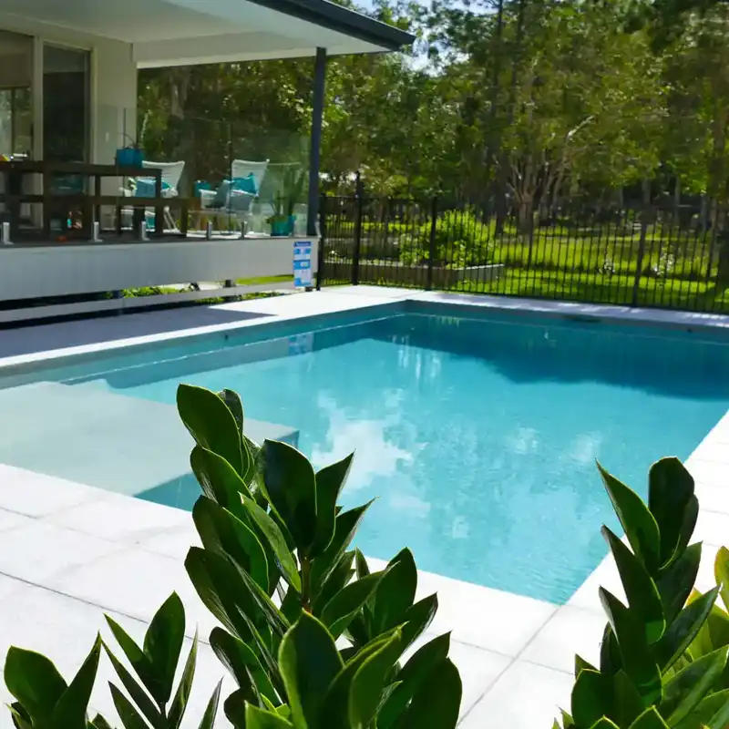 Custom concrete swimming pool with modern design, light-coloured interior and surrounding outdoor entertaining area.